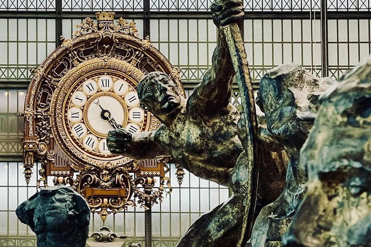 パリ・オルセー美術館の象徴である黄金の大時計をブロンズ彫刻越しに見る